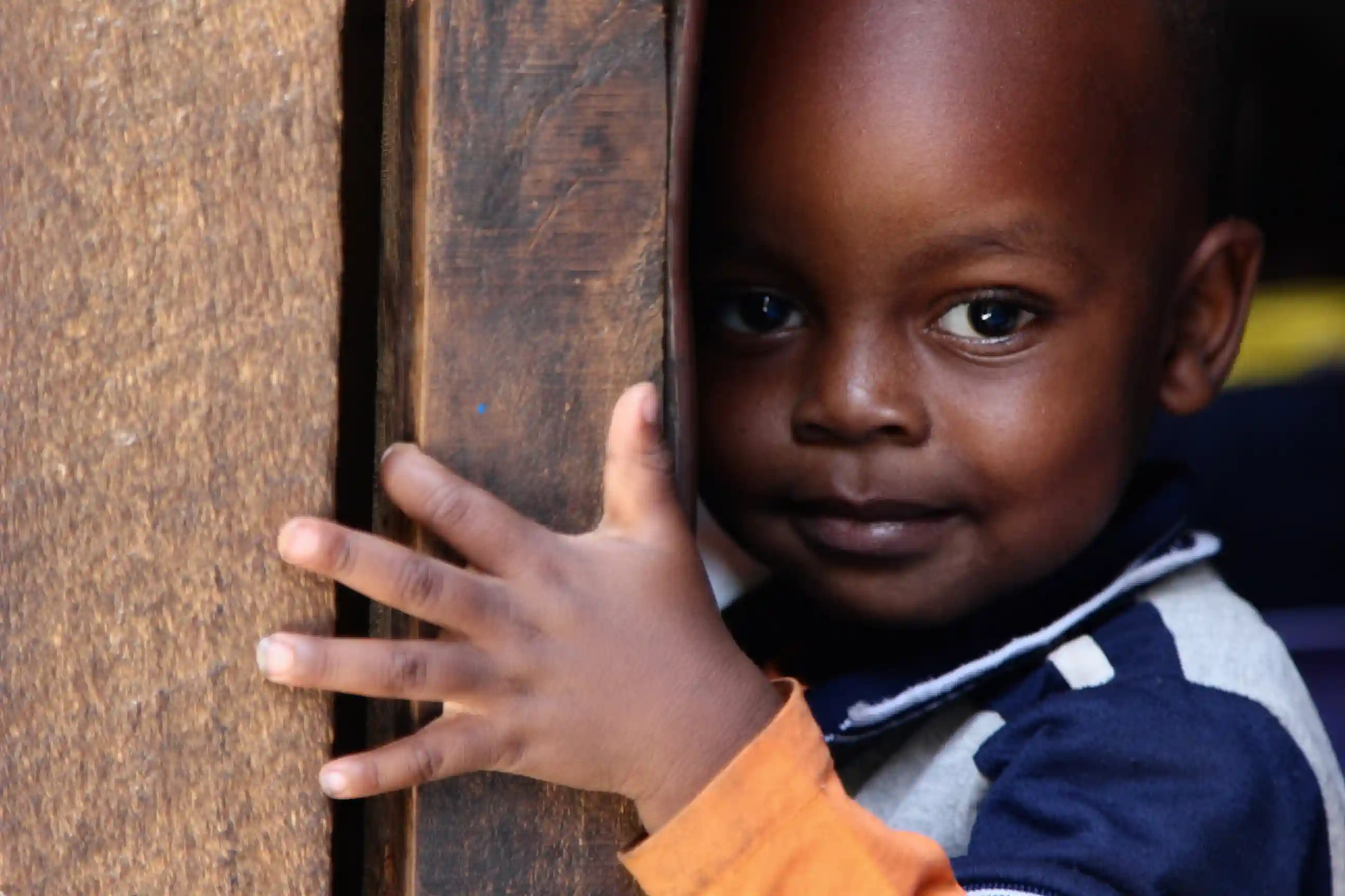 Young boy peeking out from behind a wooden wall